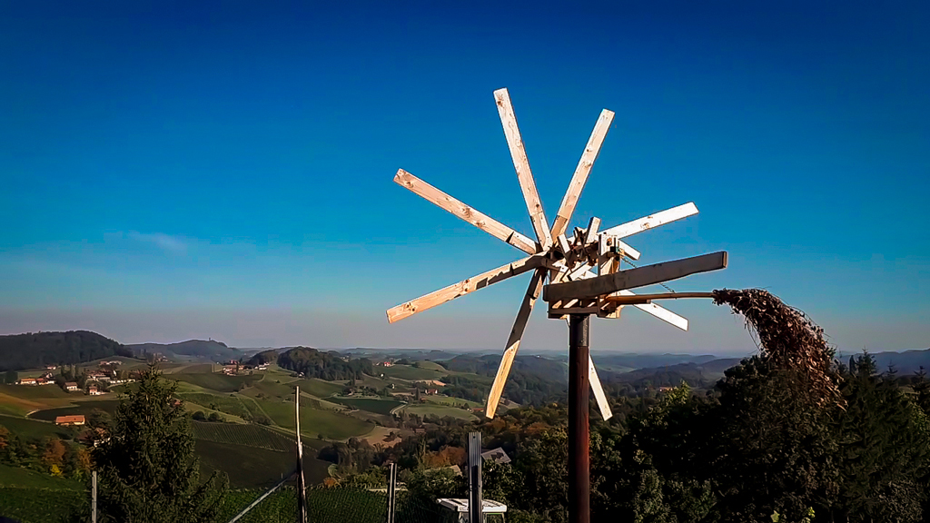 Aussicht von der Sonnenterrasse beim Samenkönig in die Südsteirische Weingegend. Im Vordergrund sieht man eine typische Klapotetz bei strahlend blauem Himmel.