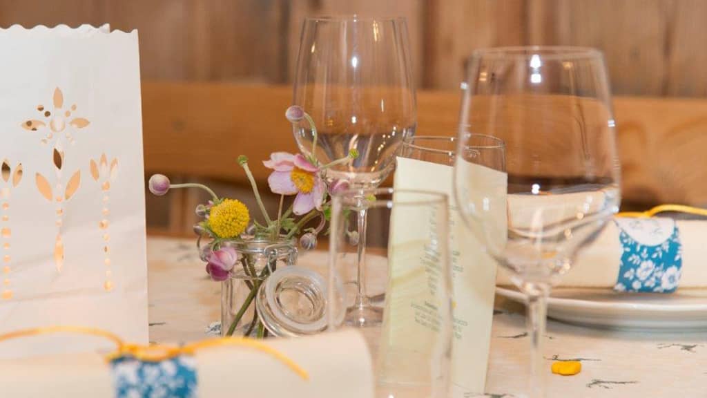 Das Bild zeigt eine Detailaufnahme eines gedeckten Tisches im urigen Buschenschank mit Weingläsern, Blumendekoration und Kärtchen.